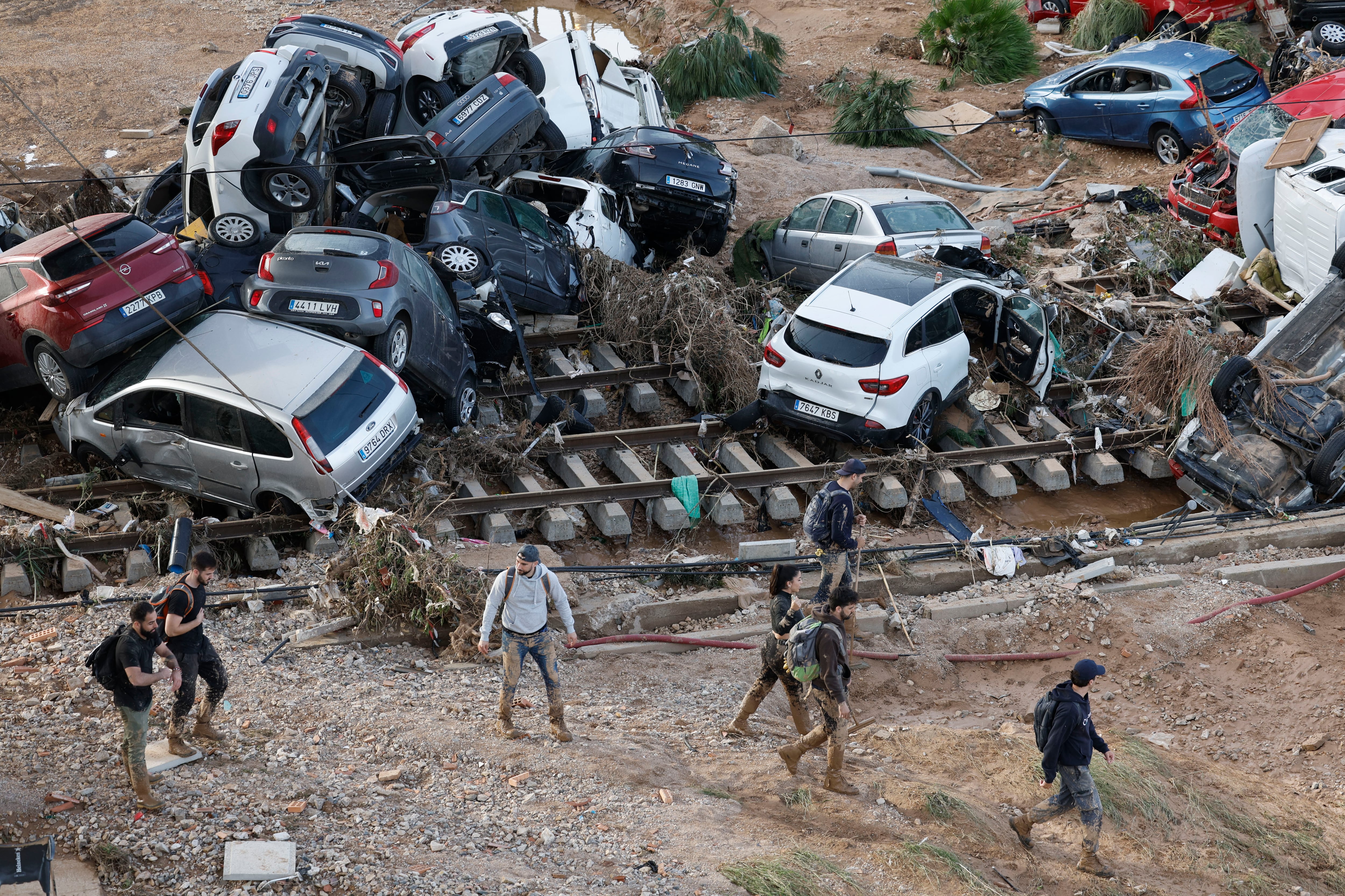 ALFAFAR (VALENCIA), 01/11/2024.- Varias personas caminan entre los vehículos apilados sobre las vías del tren en Valencia, este viernes. La búsqueda de desaparecidos, la identificación de víctimas mortales, las tareas de limpieza y la reparación de infraestructuras continúan tres días después de las inundaciones que han asolado la provincia de Valencia, en una jornada en la que el Gobierno envía a 500 militares más, que se sumarán a las 1.200 efectivos de la Unidad Militar de Emergencias (UME), para actuar en Utiel, Requena, Riba-roja, Torrent, Paiporta y Algemesí. EFE/ Kai Försterling
