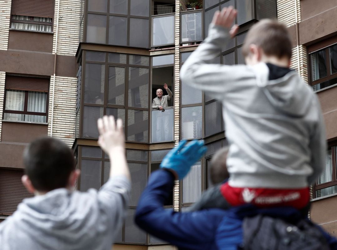 Dos niños saludan a su abuelo asomado a la ventana en una día donde acaba el confinamiento para los menores de 14 años que pueden salir a la calle.