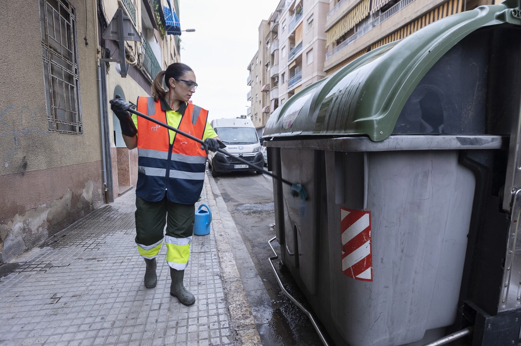 Una operaria limpia un contenedor en una calle de Gandia.