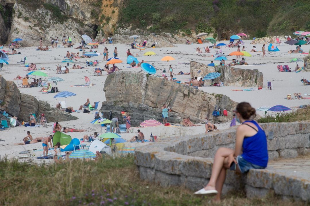 Una persona sentada frente a la playa en A Mariña