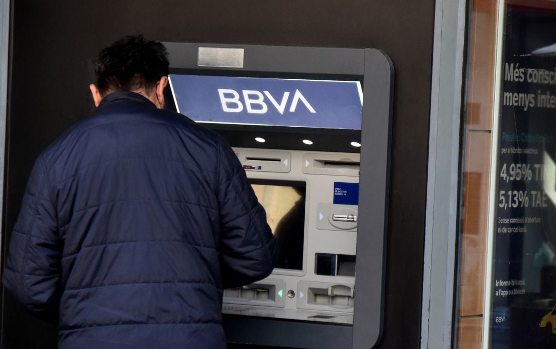 Un hombre saca dinero frente a un cajero.