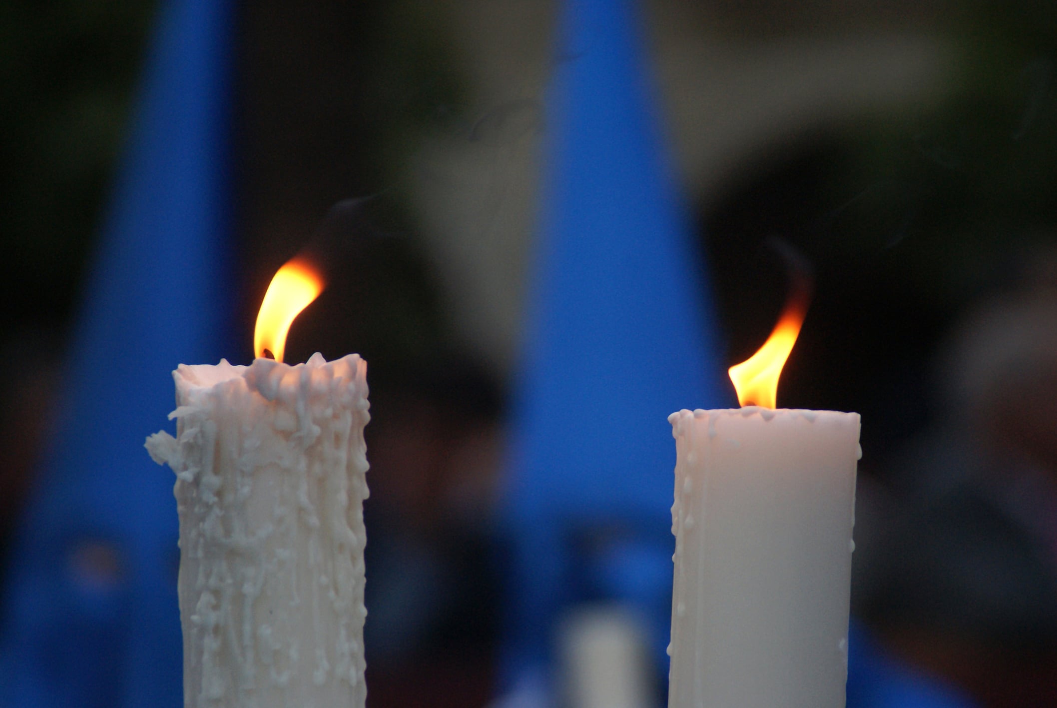 Cirios ardiendo, portados por dos nazarenos de Semana Santa con túnica azul