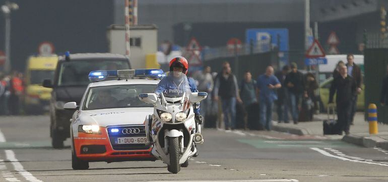 Vehículos policiales pasan al lado del edificio de la terminal tras registrarse explosiones en el aeropuerto internacional de Zaventem