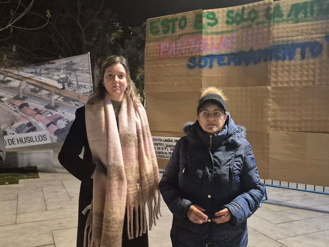 Cristina Martin Moro (i) y Maite Rodríguez (d), de la Federación de Asociaciones de Vecinos de Palencia, frente a la pantalla ficticia que han colocado frente a la estación como un acto reivindicativo y de protesta