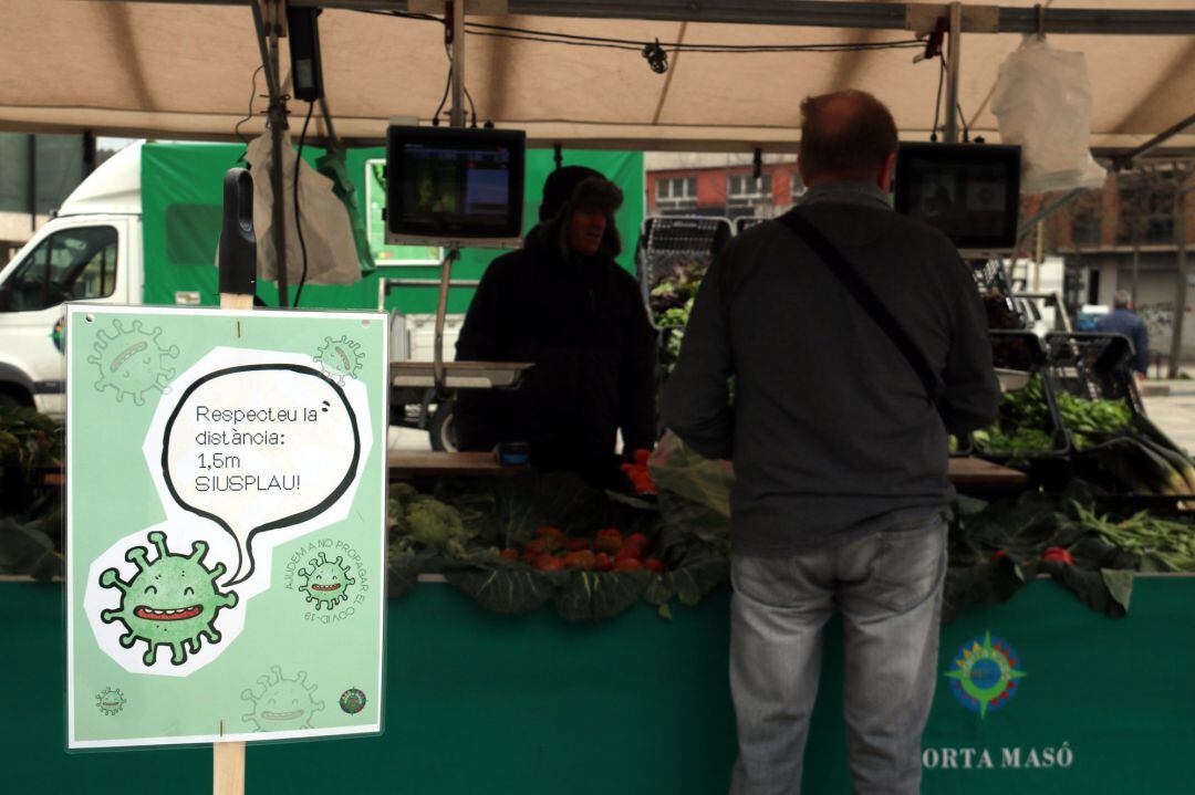 El cartell que marca la distància per al següent client a la cua en una parada de l'exterior del Mercat del Lleó de Girona, el 16 de març del 2020 (horitzontal)