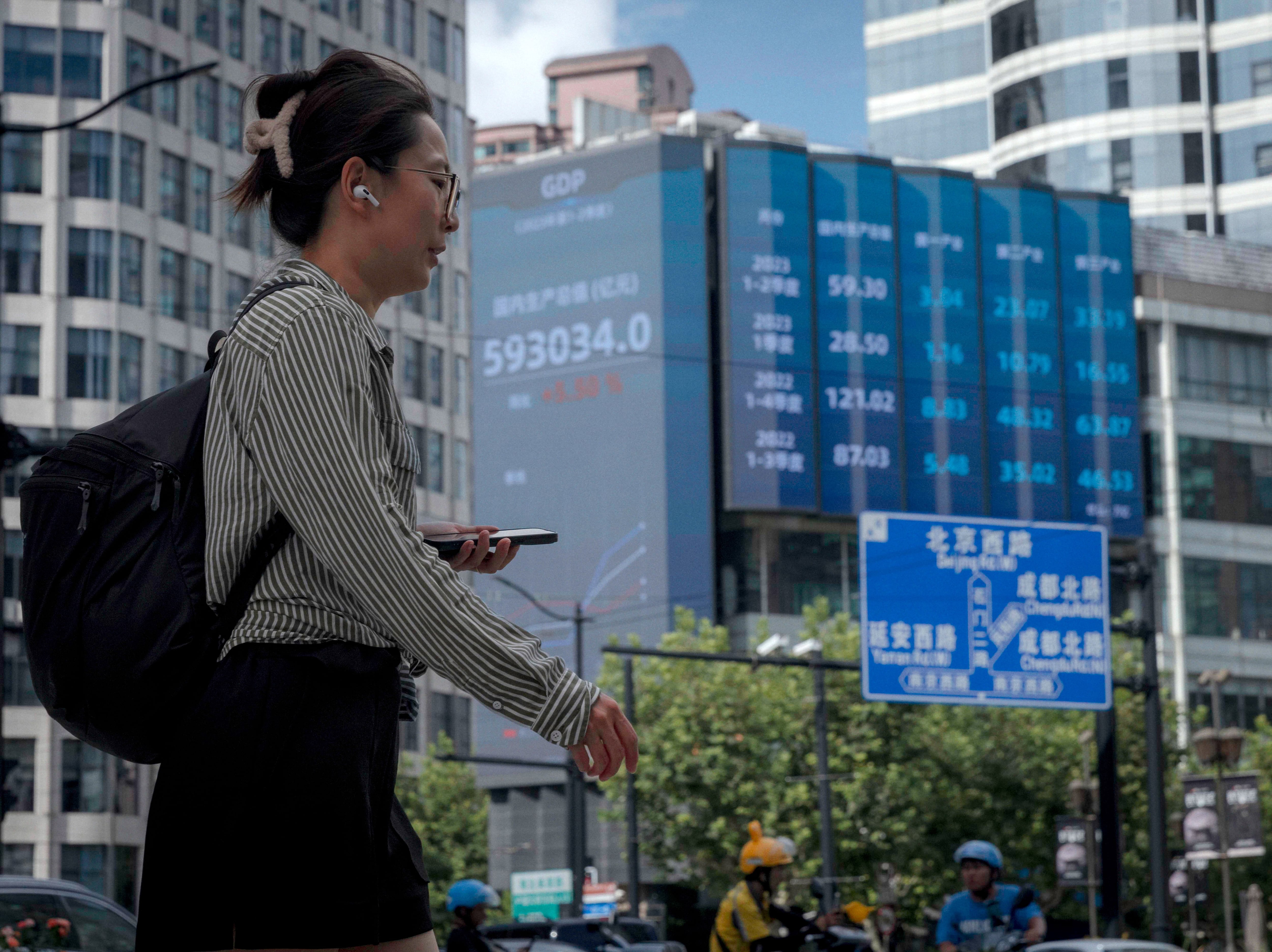 Una mujer pasea en la calle frente a la bolsa de Shanghai en China, que lleva dos días seguidos sumando pérdidas por los malos datos económicos