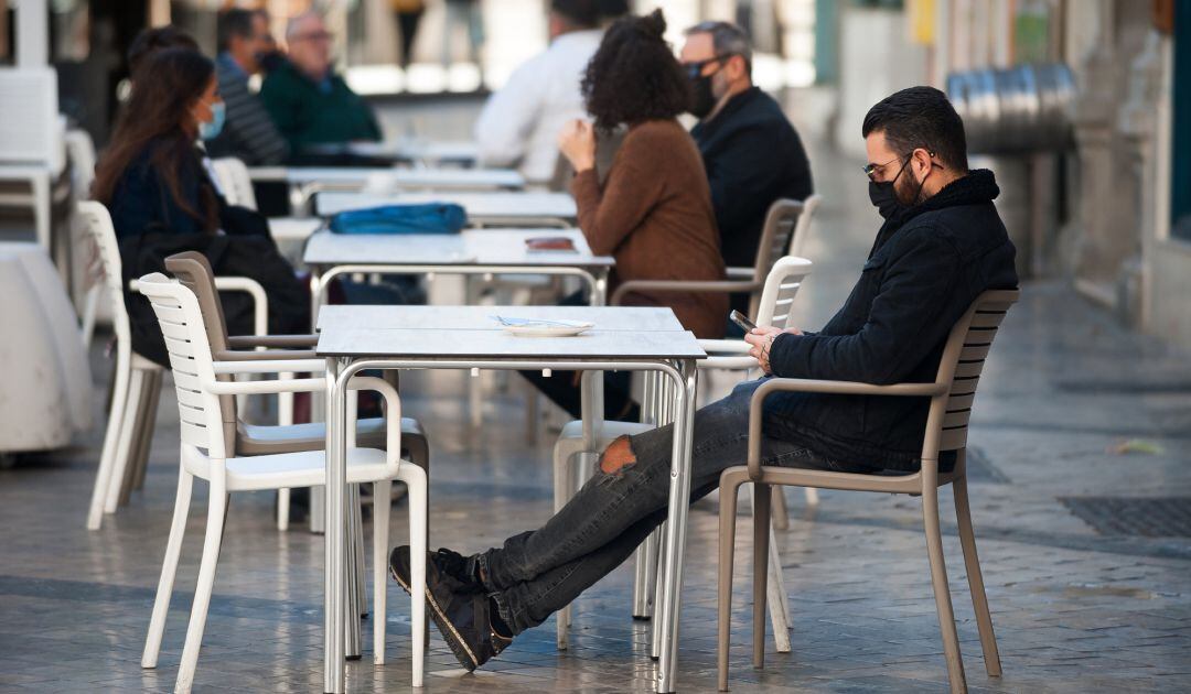 Varias personas con mascarilla sentadas en la terraza de un bar.