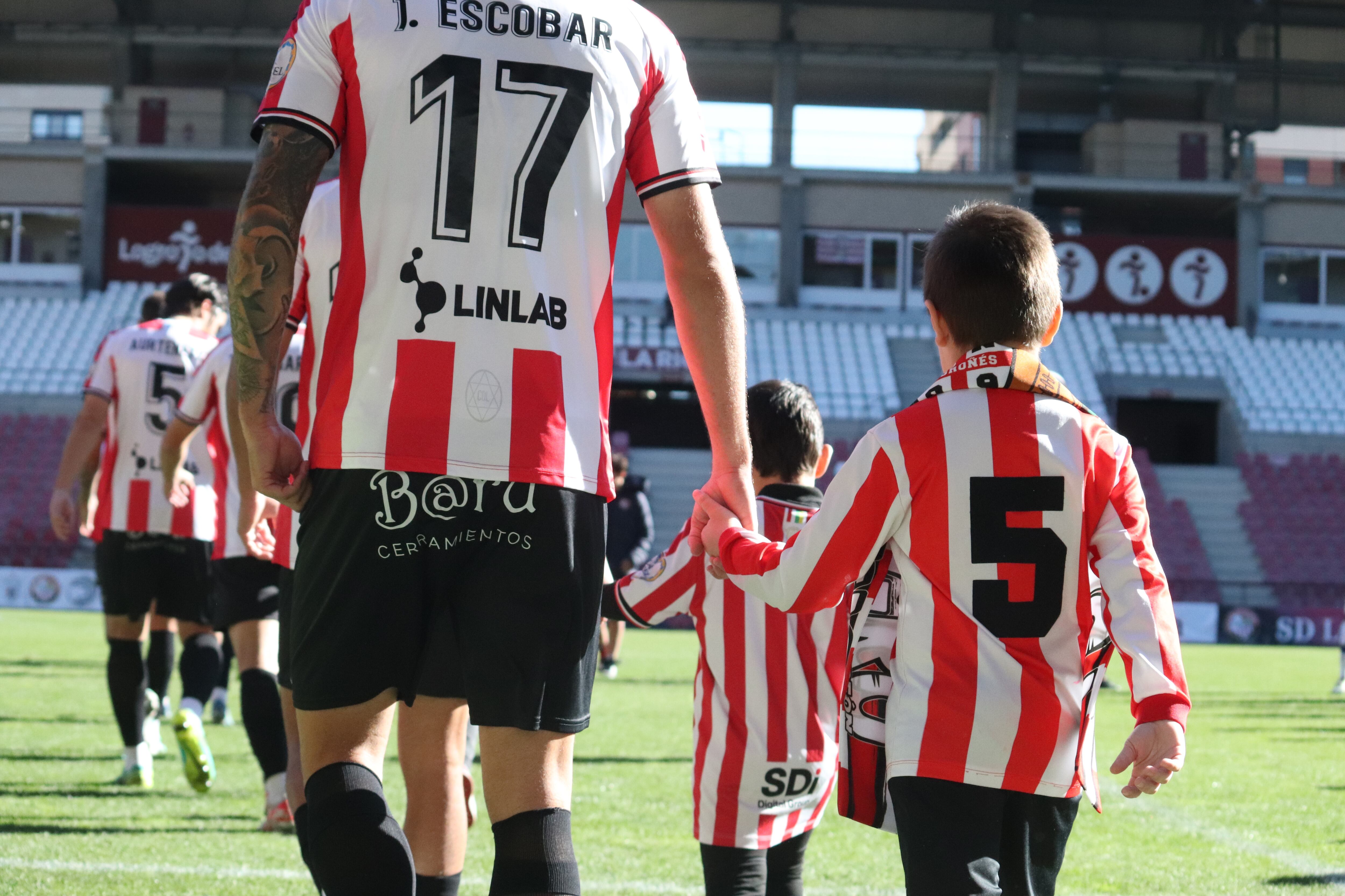 Jordi Escobar salta al césped de Las Gaunas junto a un joven aficionado blanquirrojo / SD Logroñés