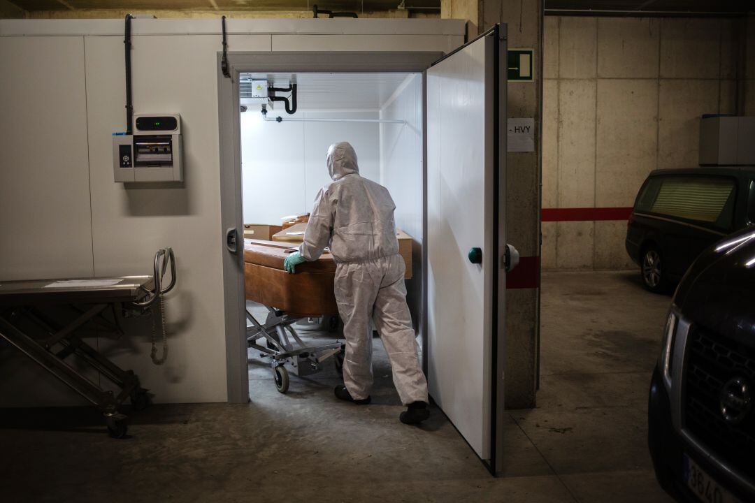 Un trabajador de una funeraria con traje de seguridad traslada el cadáver de un fallecido por COVID-19.