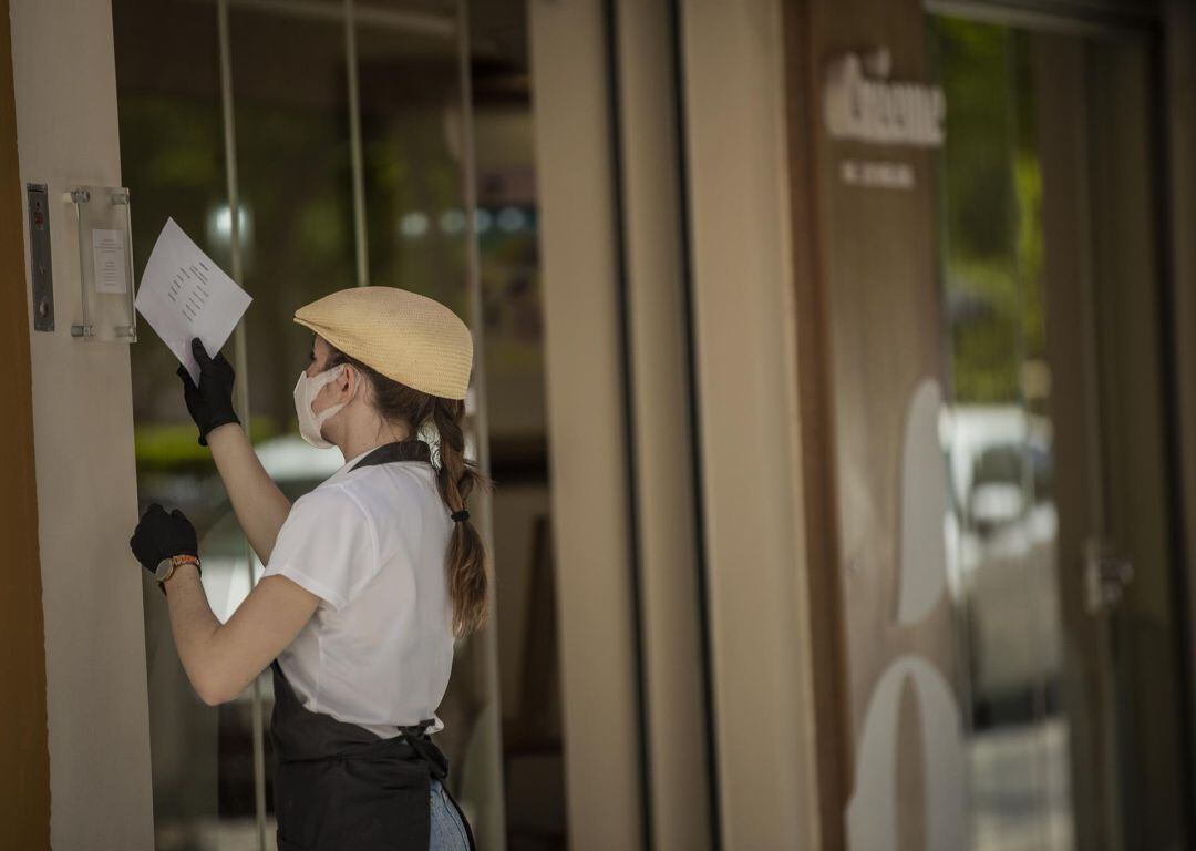 La empleada de una heladería colocando un cartel con el nuevo horario