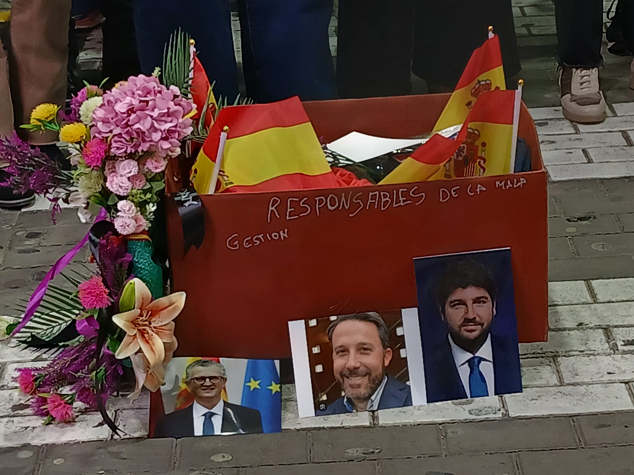 Una manifestante acude a una protesta sanitaria con una corona de flores y coloca la fotografía de responsables políticos