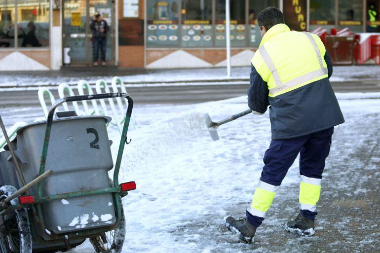 Un operario esparce sal en una calzada con nieve y hielo