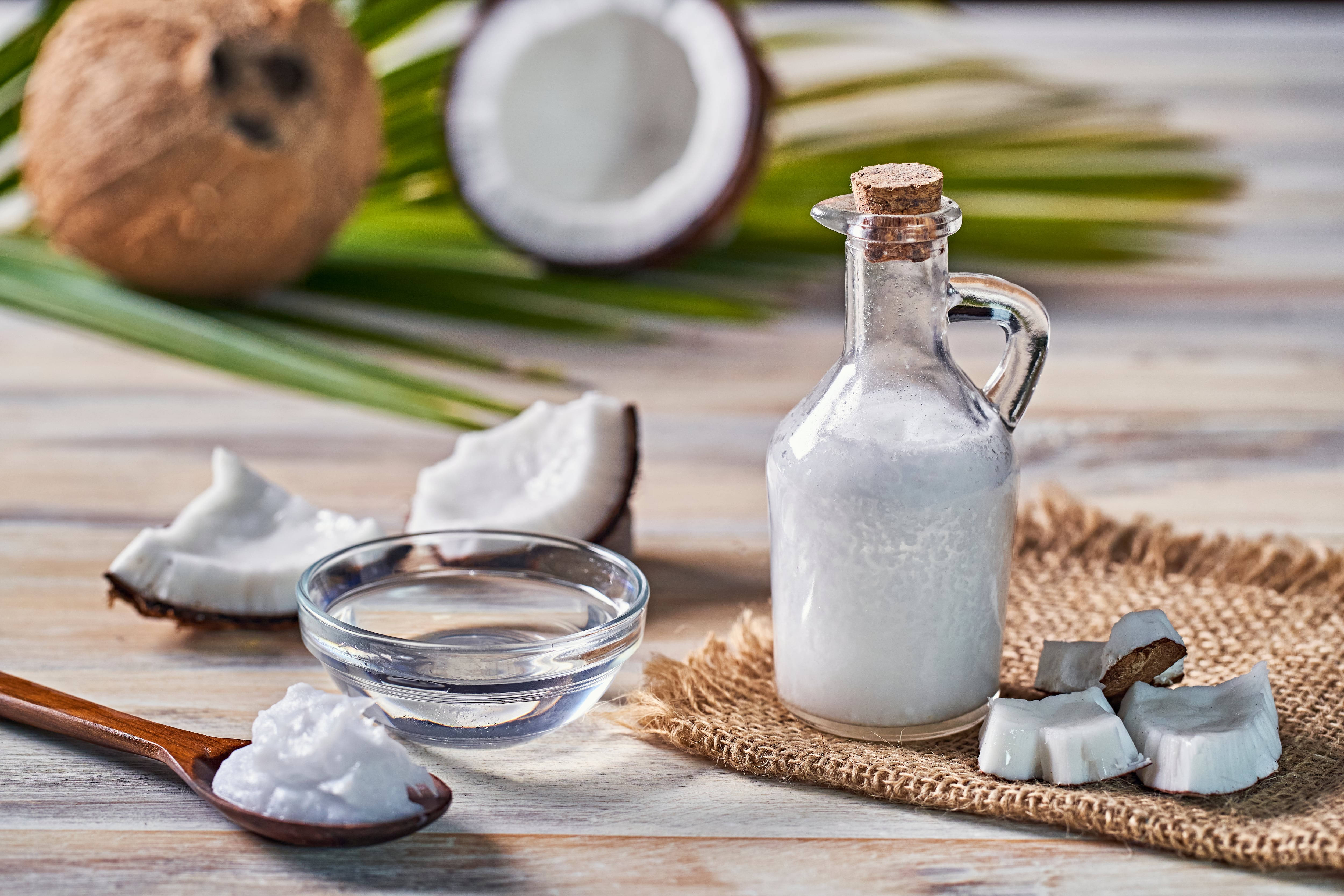 Glass bottle of coconut oil and fresh coconut fruit on wooden rustic white background, alternative therapy medicine concept