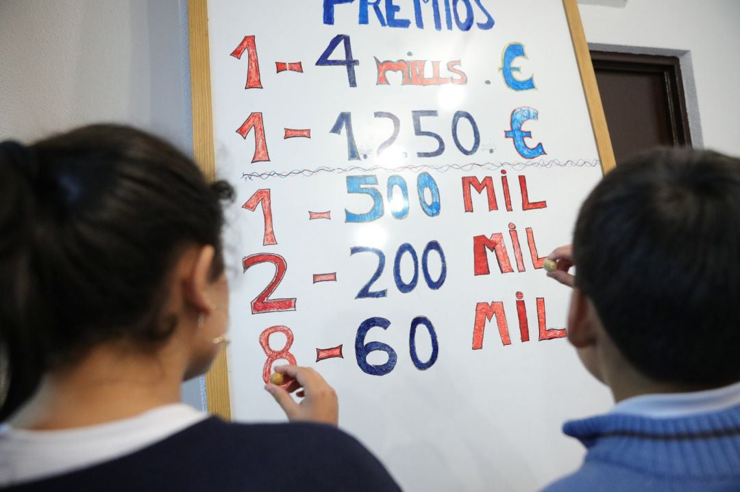 Dos niños de la Residencia Internado San Ildefonso apuntan en una pizarra el número de premios y la cantidad correspondiente a cada uno, preparándose para la celebración del Sorteo de la Lotería de Navidad del próximo 22 de diciembre.