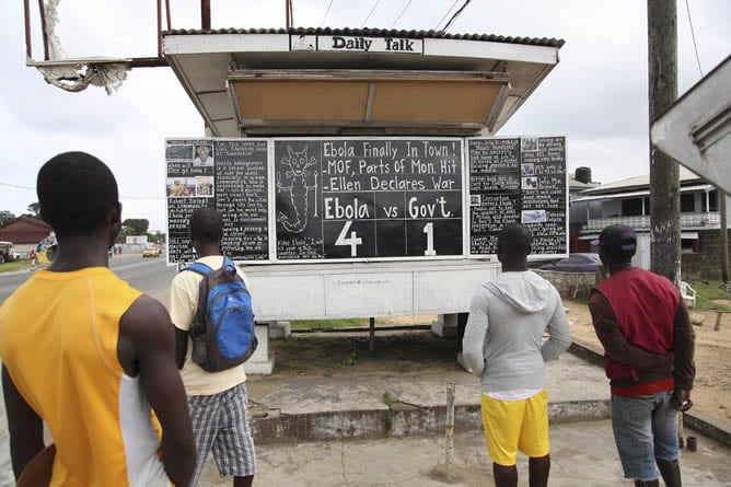 Un grupo de personas observa el tablero que anuncia la cifra de víctimas mortales de Ébola en el país, en una valle de Monrovia (Liberia)