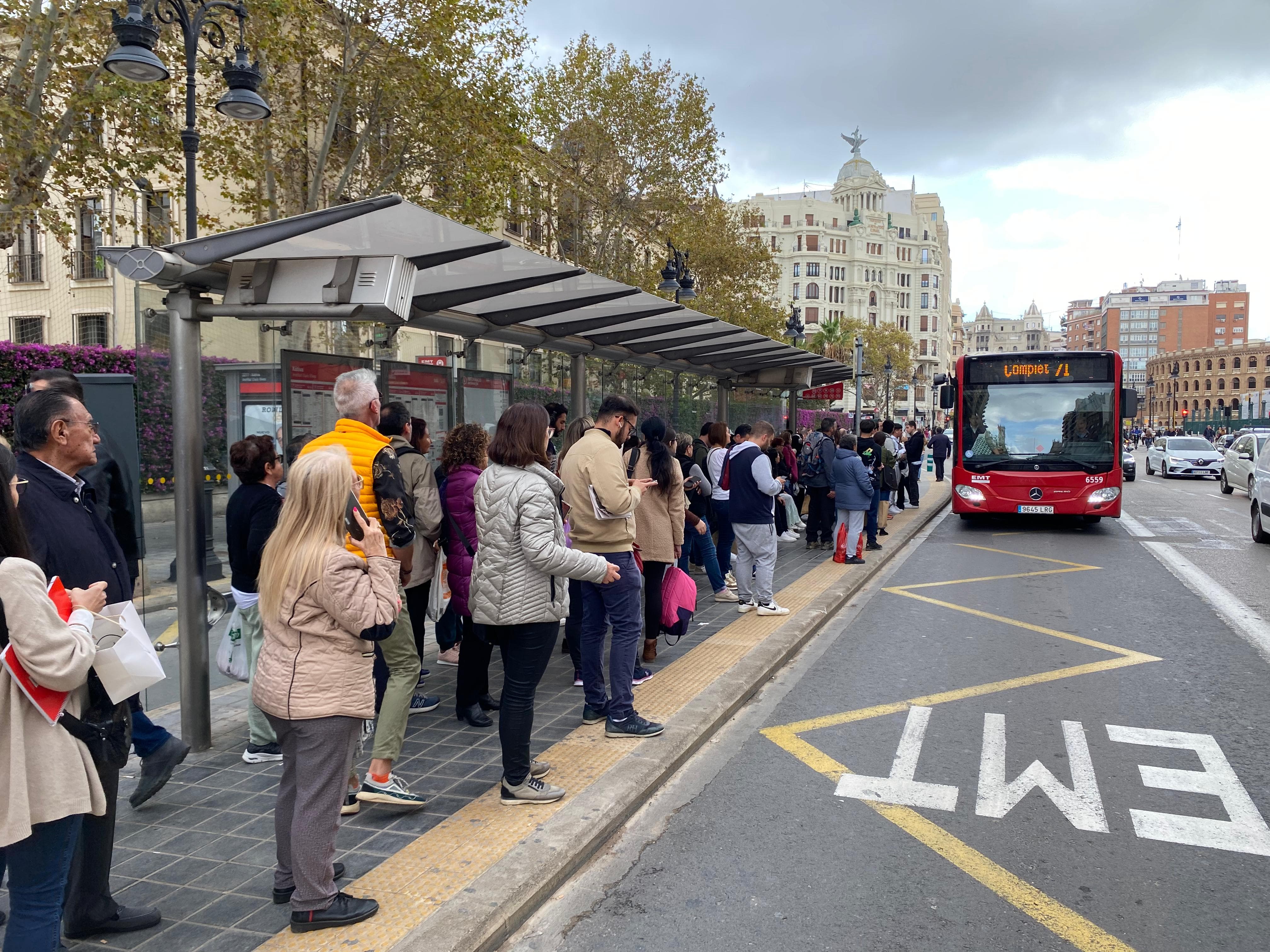 Pasajeros esperan a un autobús de la EMT que llega completo.