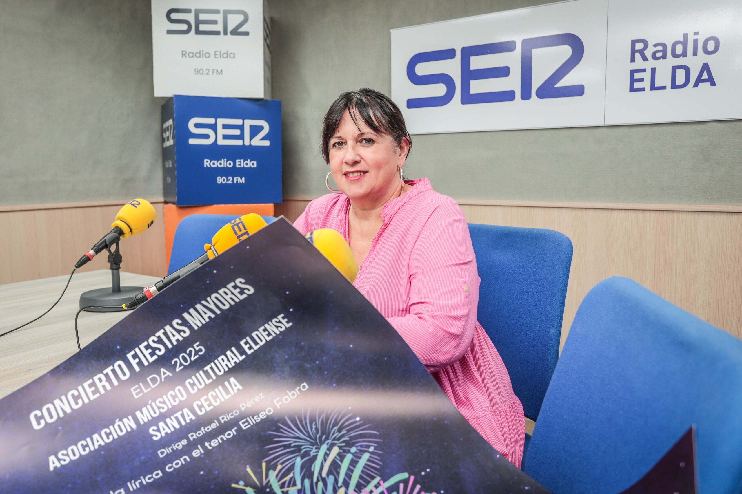 Loli Soler, presidenta de la Asociación Musical Cultural Santa Cecilia junto al cartel anunciador