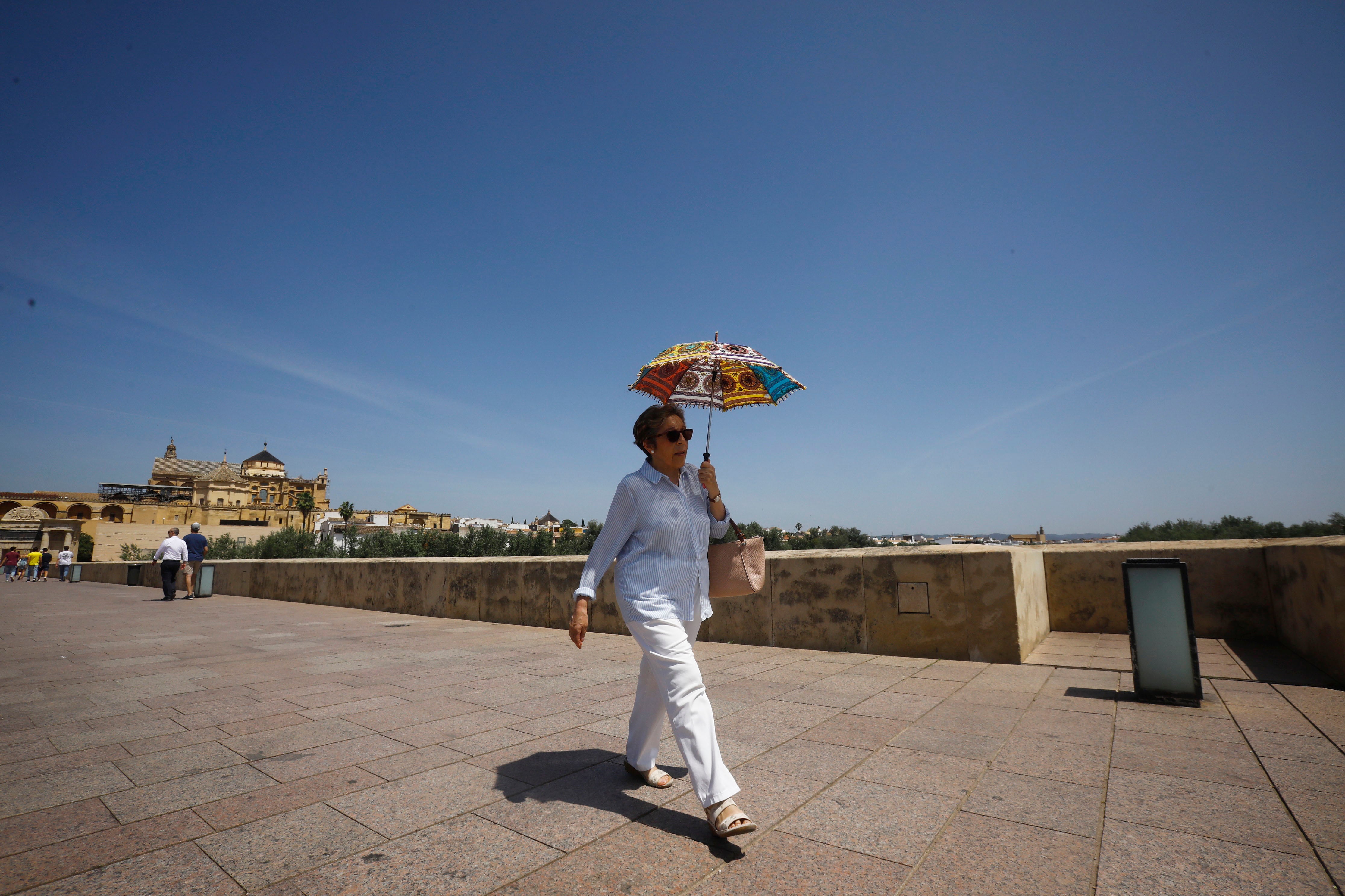 Una mujer se protege con un paraguas del intenso calor mientras pasea este jueves por el puente romano de Córdoba.