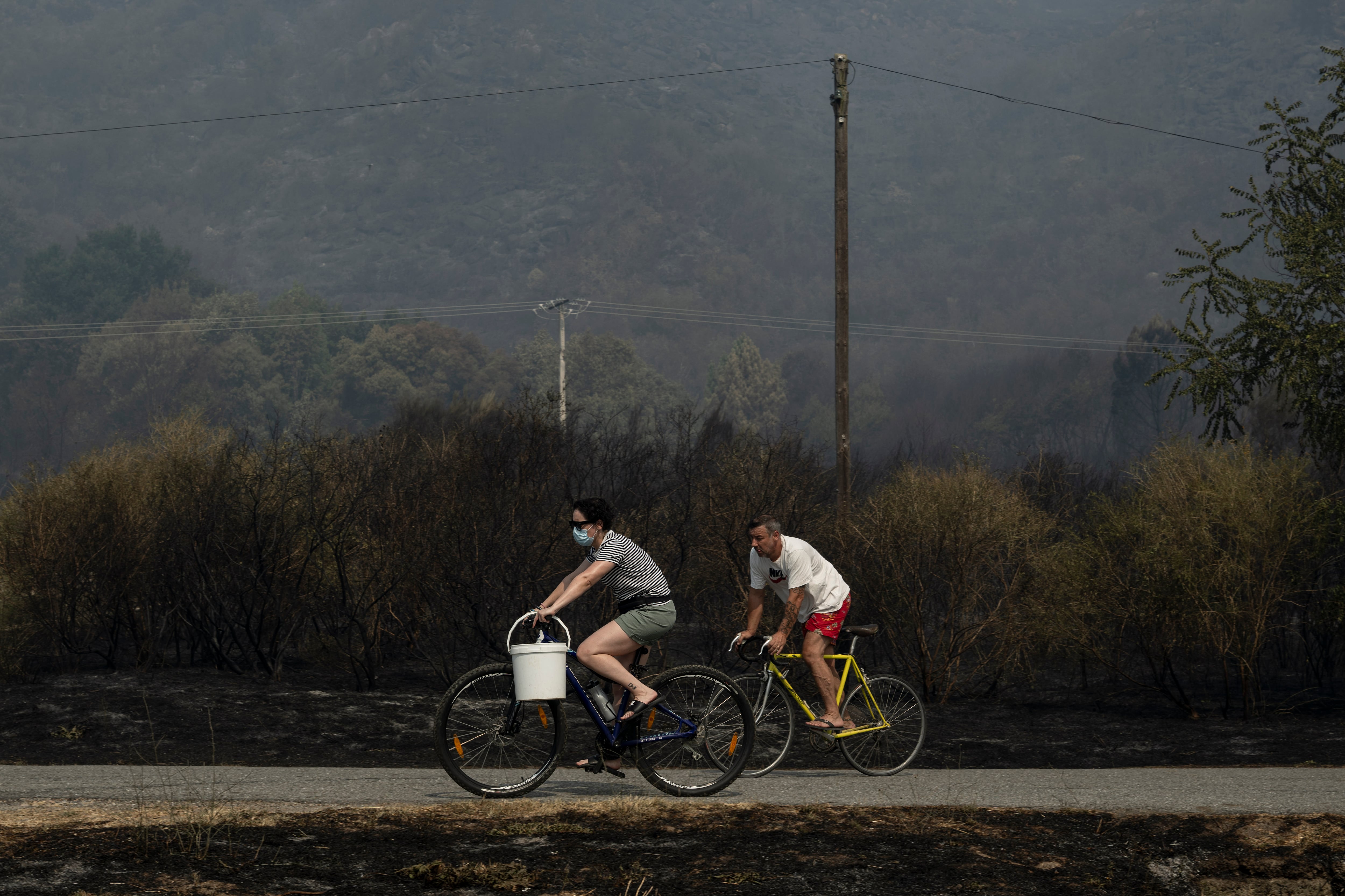 MONTERREI (OURENSE), 14/08/2025.- Dos personas, una de ellas protegida con una mascarilla, circulan en bicicleta por una zona quemada debido al incendio de Monterrei (Ourense).
EFE /Brais Lorenzo