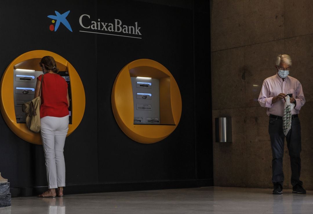 Dos personas en los cajeros dispuestos en el edificio de la sede de Caixabank, en Valencia