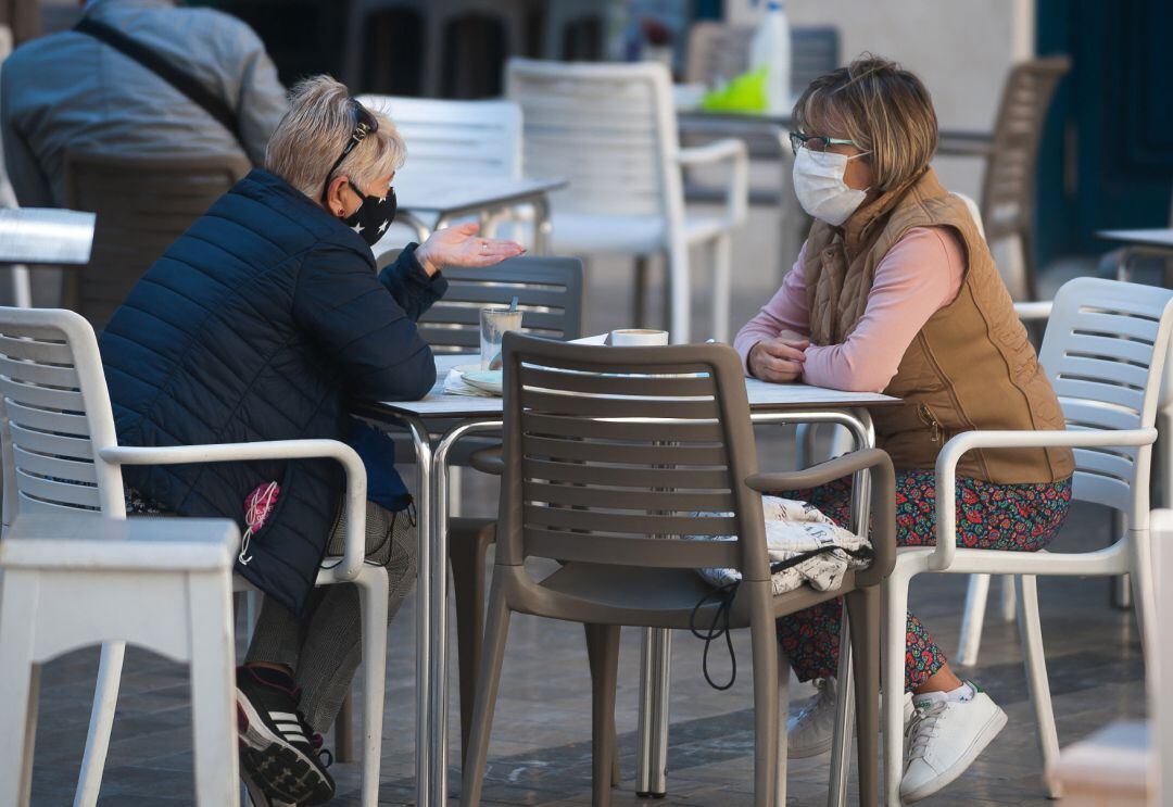 Dos mujeres con mascarillas sentadas en la terraza de un bar.