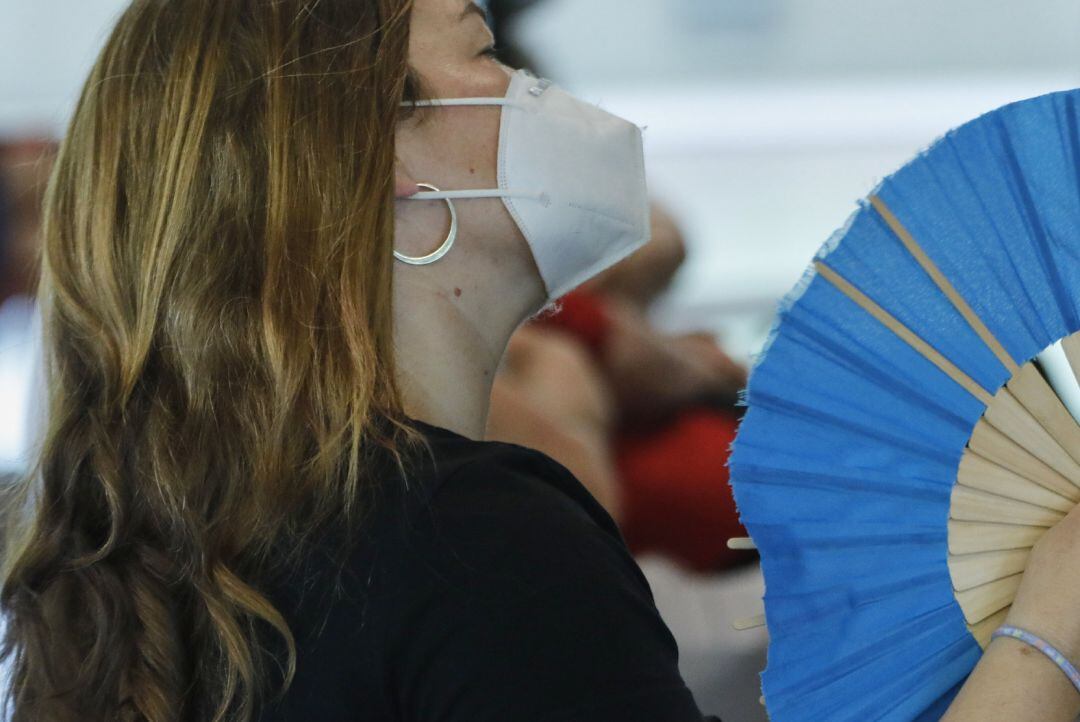 Una mujer con mascarilla se abanica.