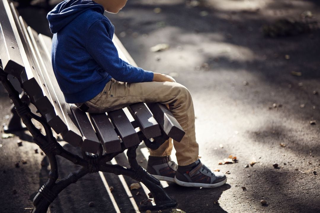 Un niño con espectro de autismo, en el banco de un parque.