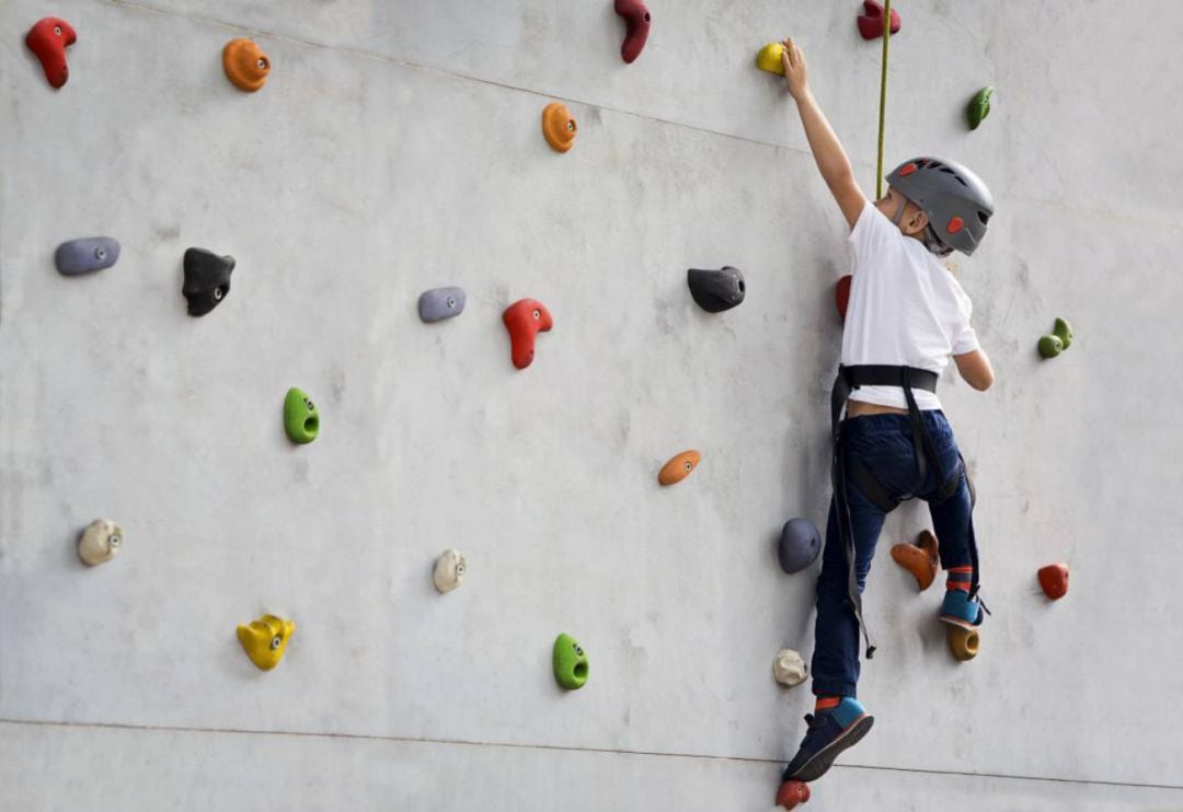 Un niño practica escalada en la pared de un rocódromo