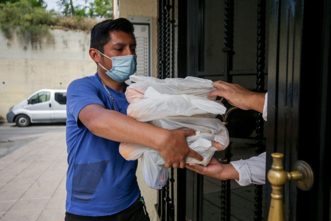 Una persona con mascarilla realiza una entrega a domicilio de alimentos en un programa solidario.