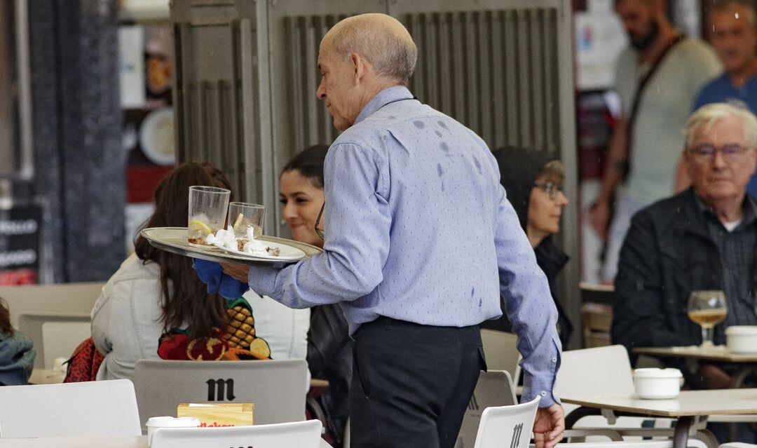 Un camarero porta una bandeja en una terraza de un bar.