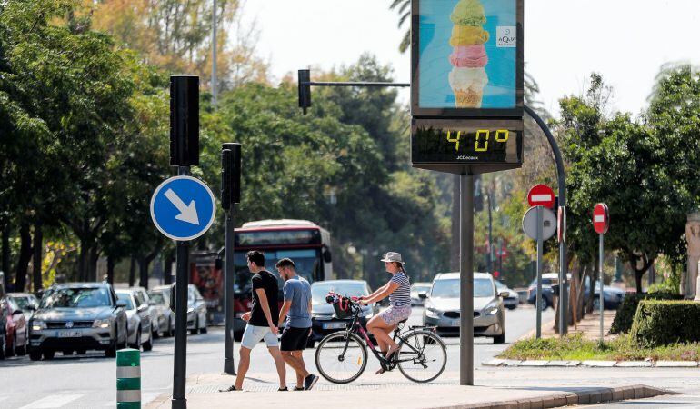 Varias personas pasan, este mediodía en la ciudad de Valencia, ante un termómetro urbano que marca una temperatura de 40º acompañados por la sensación de bochorno