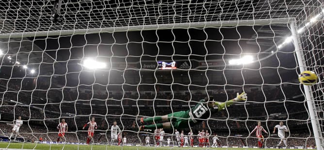 El portero belga del Atlético de Madrid Thibaut Courtois trata de detener el lanzamiento del portugués Cristiano Ronaldo, del Real Madrid, durante el partido de Liga que se disputó este sábado en el estadio Santiago Bernabéu, en Madrid y en el que venció 