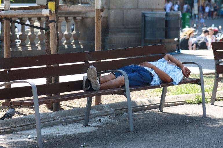 Un home dormita en un banc de la Plaça Catalunya de Barcelona, a migdia 