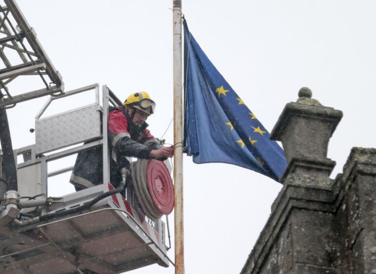 Los Bomberos de Santiago colocan la bandera de la Unión Europea a media asta, en el tejado del ayuntamiento, por decisión de la alcaldía y para manifestar el rechazo a la política de la UE respecto a los refugiados, esta mañana en la plaza del Obradoiro e