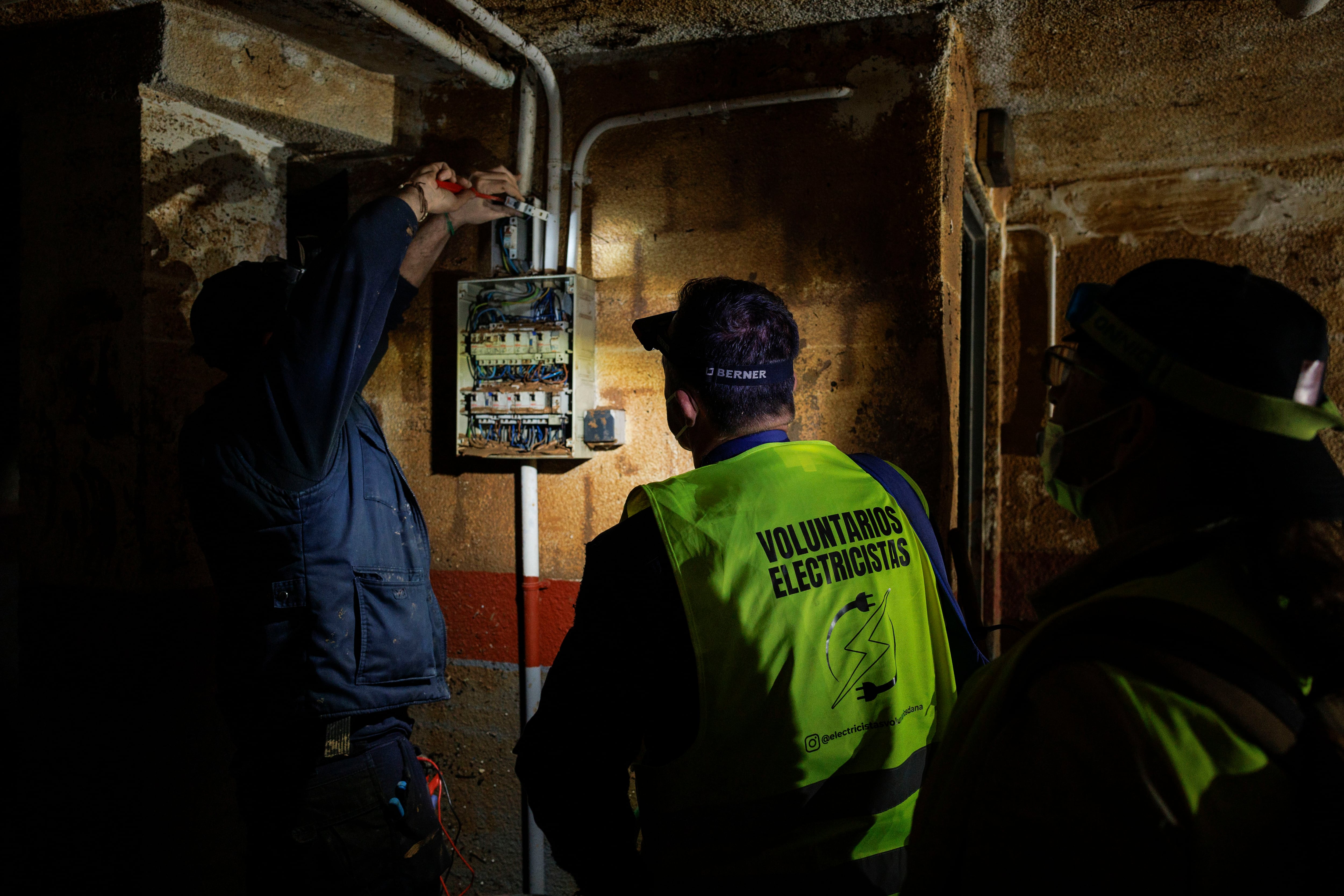 Dos electricistas voluntarios trabajan en un garaje de Catarroja para restablecer el suministro eléctrico que perdieron tras la DANA.