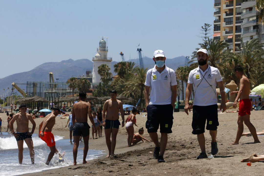 Una pareja de Vigilantes de la playa de Andalucía asesoran a bañistas sobre las medidas preventivas sobre el COVID-19 en la playa de La Malagueta. Málaga a 16 de junio del 2020