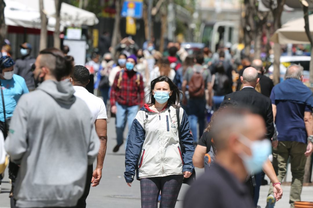 Varias personas caminan por el centro de una ciudad llevando mascarilla