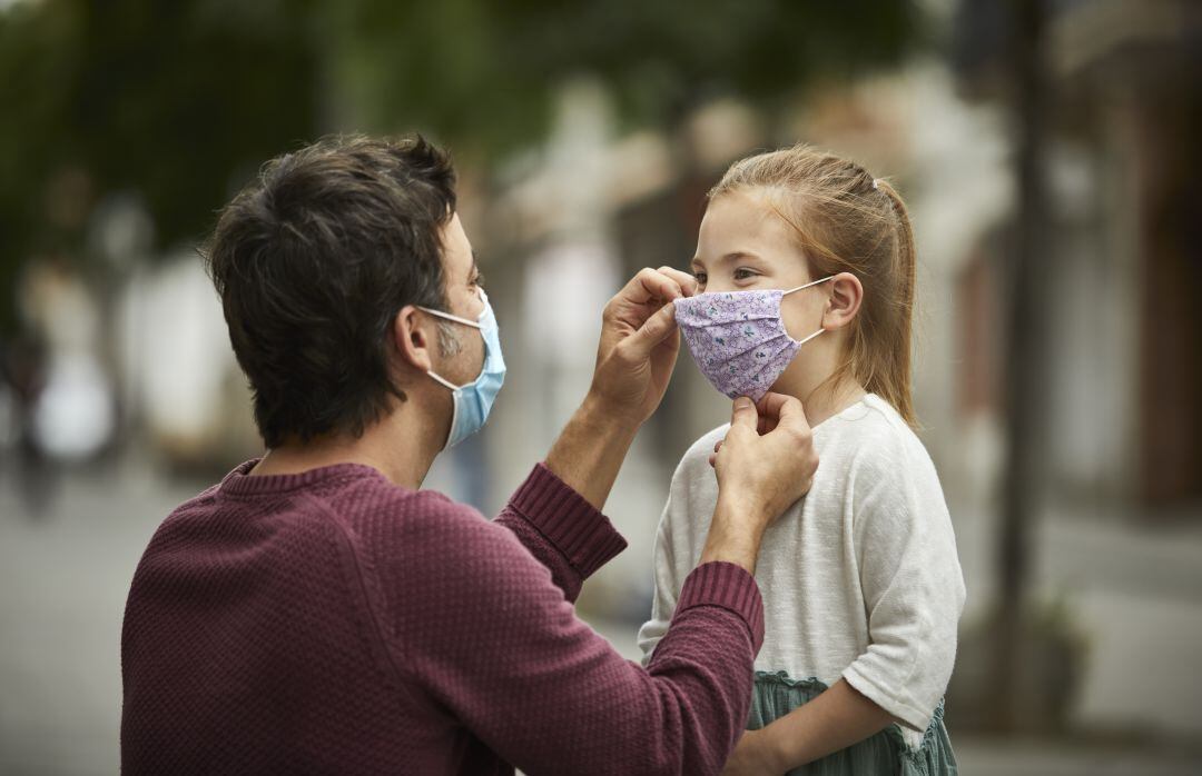 Un padre coloca una mascarilla a su hija en el exterior.