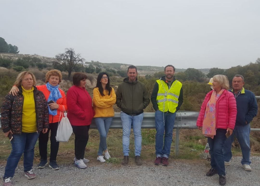 Juan Antonio Carrión, encadenado al puente cortado sobre el río Baza, acompañado por vecinos de Benamaurel y miembros de la plataforma que pide una solución provisional para la movilidad en la comarca. A la derecha del encadenado, además, el alcalde de Benamaurel, Juan Francisco Torregrosa