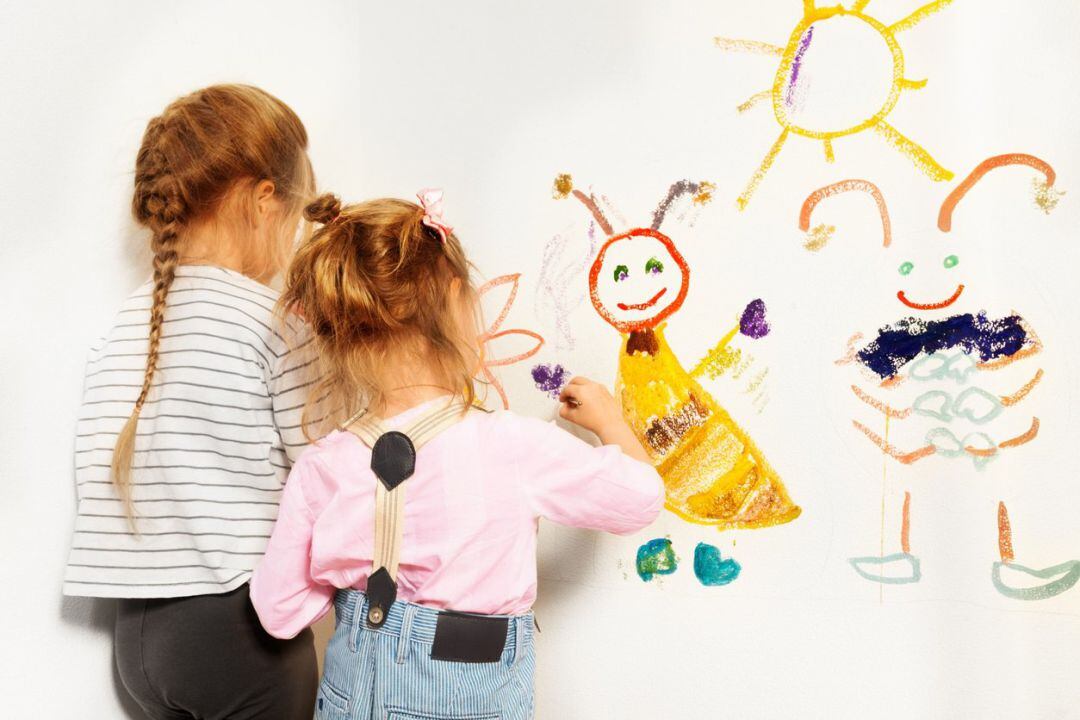 Dos niñas pintando en la pared de una escuela infantil.