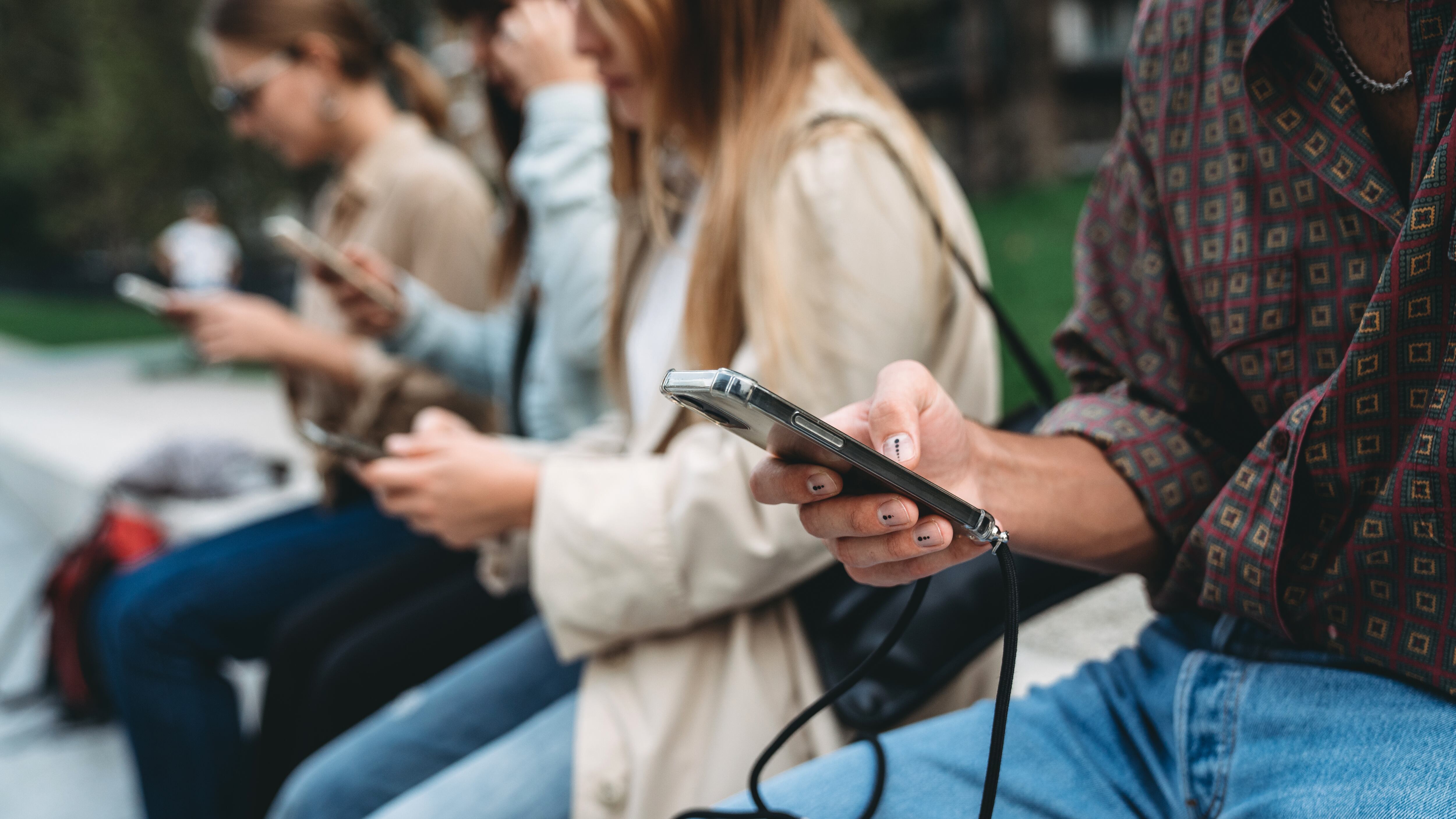 Varias personas consultan información en sus teléfonos móviles.