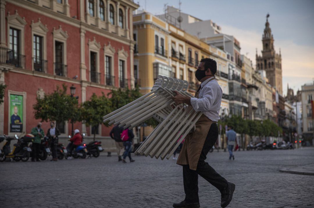 Un hostelero recoge el mobiliario de la terraza de un bar, tras la nueva medida de restricción que obliga al cierre de toda actividad no esencial a partir de las 18,00 horas.