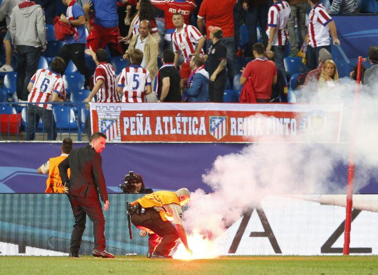 Operarios retiran una bengala del terreno de juego durante el partido de la Liga de Campeones entre Atlético de Madrid y Benfica