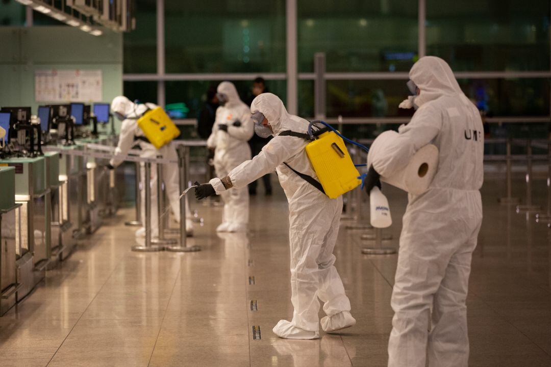 Cuatro agentes de la Unidad Militar de Emergencias (UME) del Ejército limpian el suelo durante las tareas de desinfección en el Aeropuerto de El Prat.