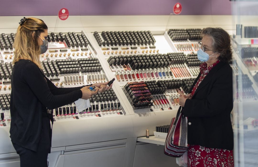 Una empleada de una tienda de cosmética atiende a una clienta manteniendo la distancia de seguridad.