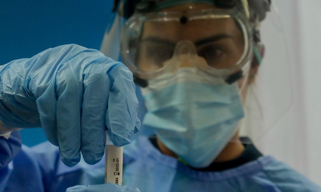 Una trabajadora sanitaria sostiene una probeta con una prueba PCR.