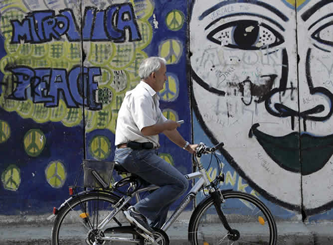 Un ciclista pasa por delante de un grafiti en la ciudad de Mitrovica, al norte de Kosovo. (Reuters)