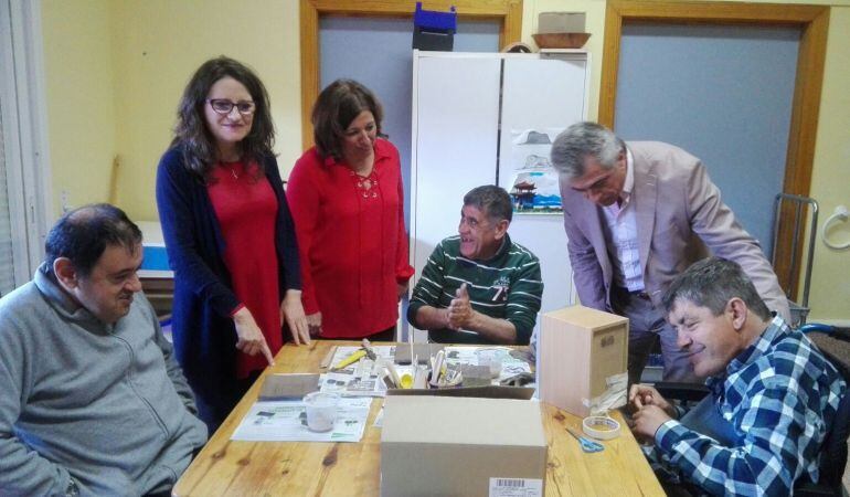 La consellera Mónica Oltra (i), junto a la directora del Centro San Rafael, Ana Carratalá, (d) en la visita a uno de los talleres.