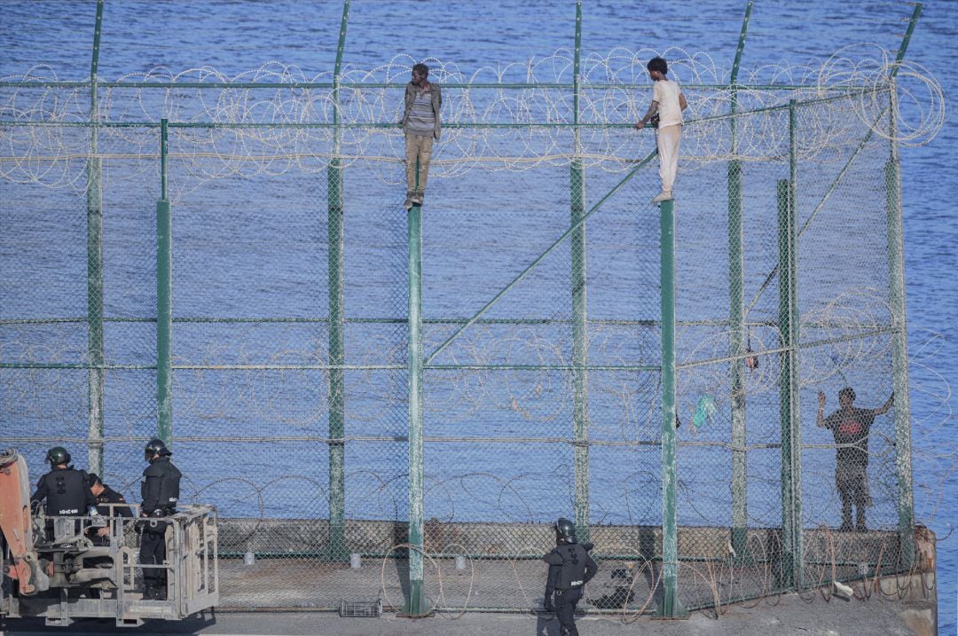 En la imagen, tres de un total de 153 migrantes, entran en Ceuta saltando su doble valla en la primera incursión en grupo en un año.