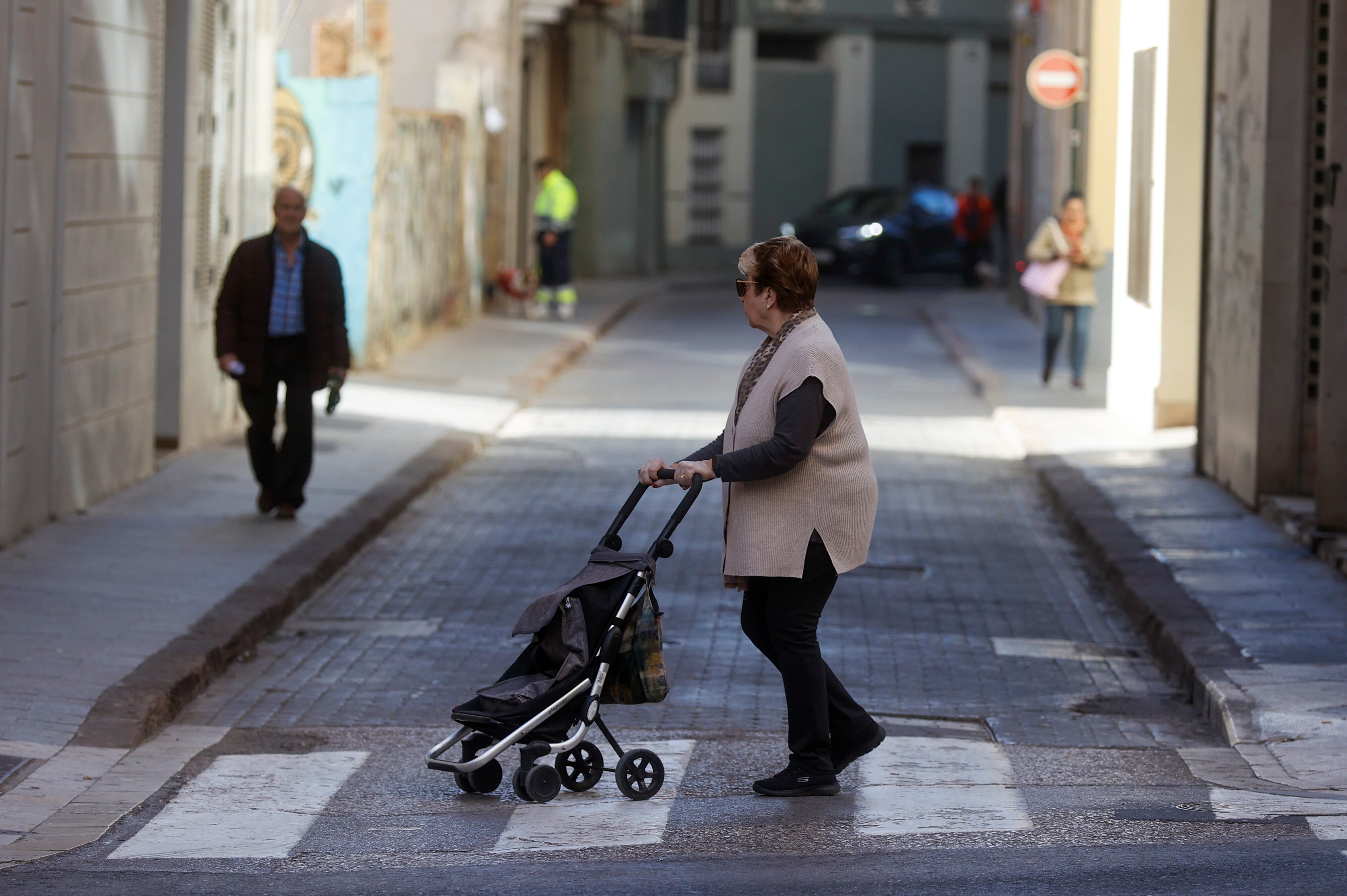 Una mujer empuja su carro de la compra camino del mercado en una calle de València